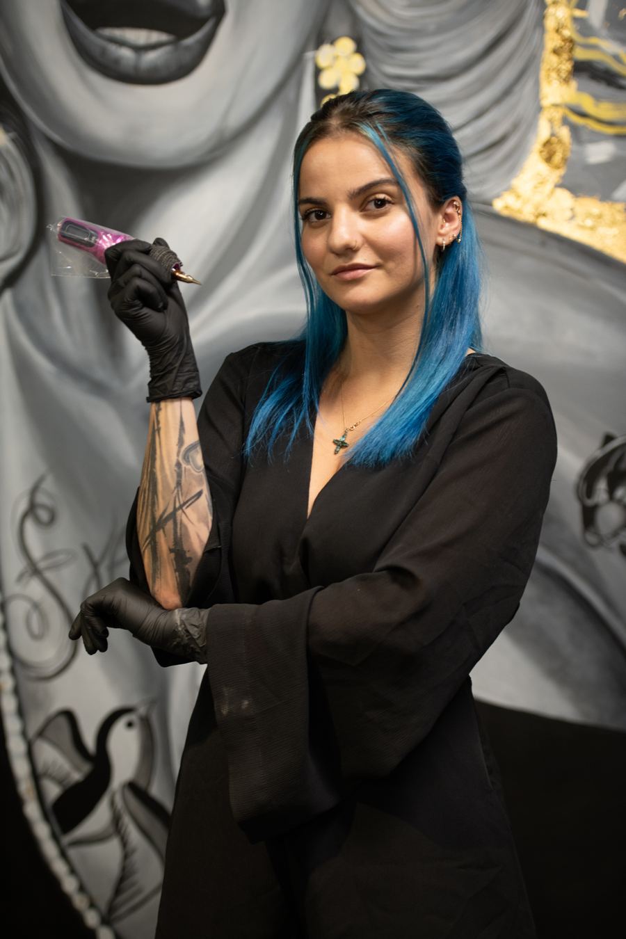 Anabelle Tremblay, machine à tatouer en main, devant la murale du studio