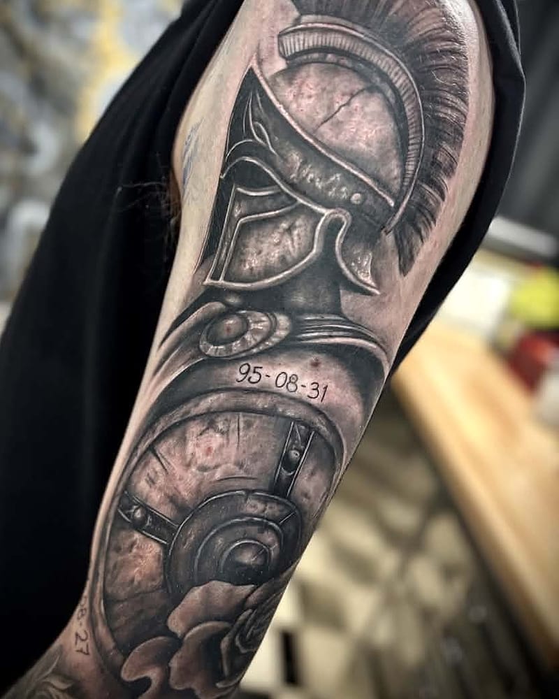 Casque de spartiate et bouclier en réalisme black and grey sur le bras, avec dates commémoratives