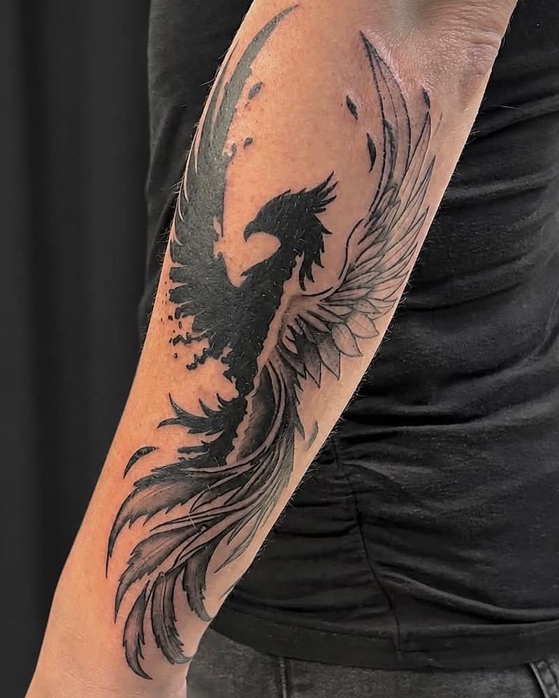 Phénix aux ailes déployées, encre noire et plumes en fineline sur l'avant-bras