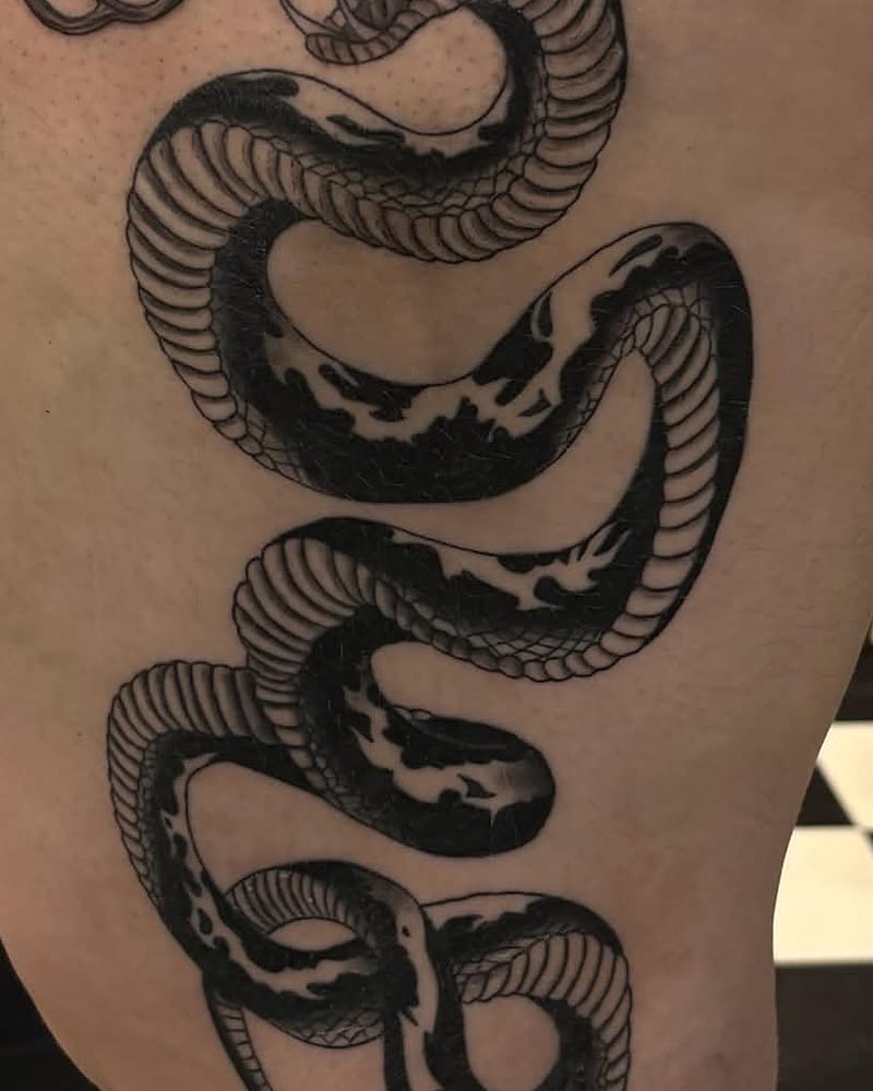 Grand serpent ondulant, gueule ouverte, en noir et gris sur la cuisse